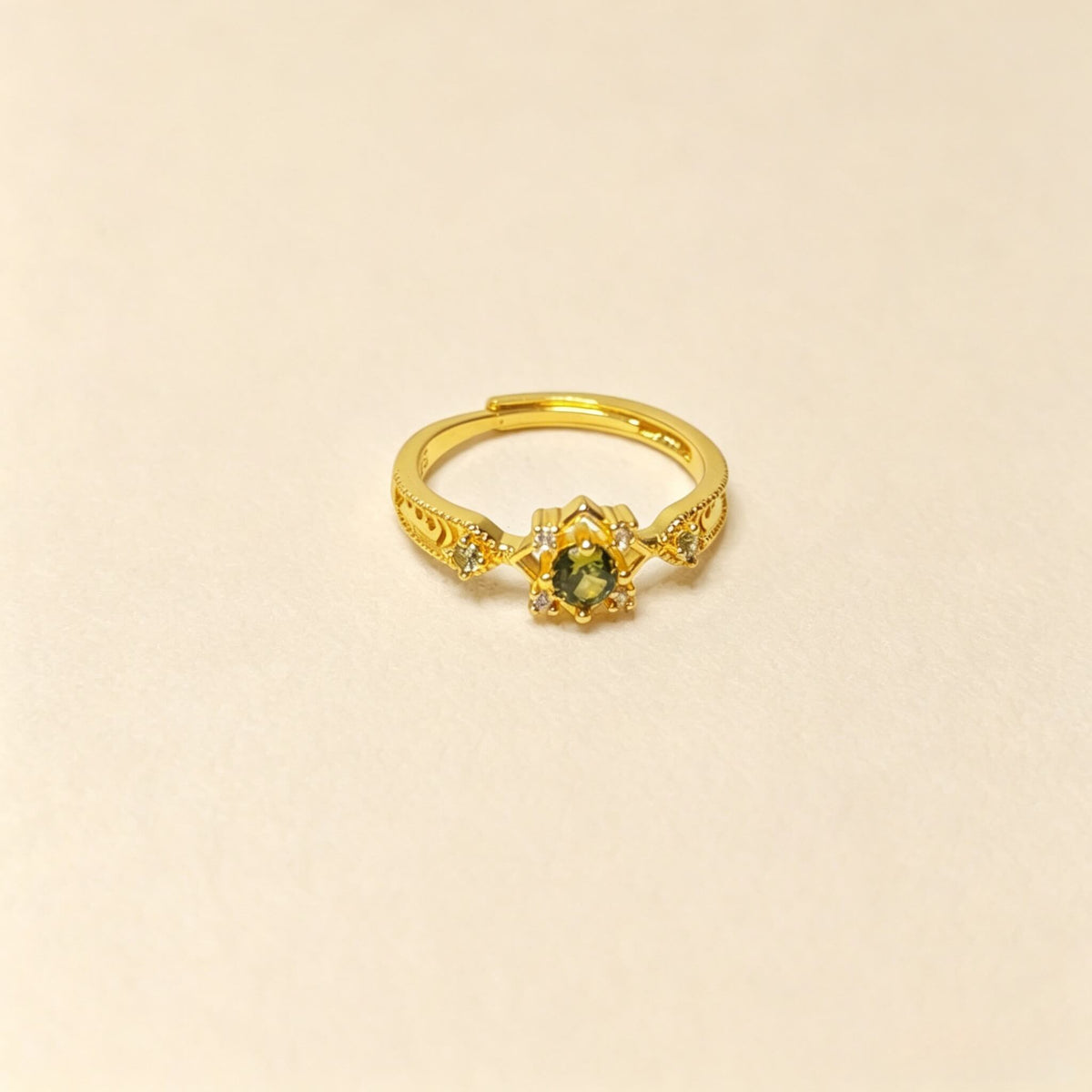 A gold ring with a central green gemstone and small accent stones, shown on a plain beige background.