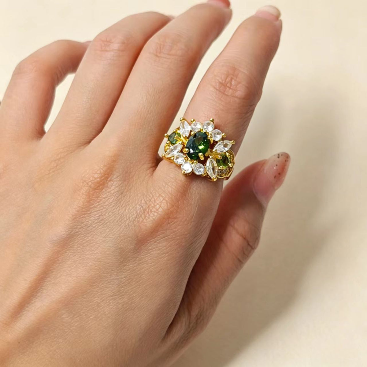 Female hand model wearing gold plated copper ring, green stone floral ring
