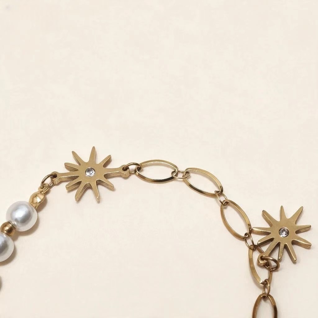 Close up of sunburst star charms, PVD gold plated stainless steel bracelet with faux pearl details
